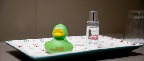 A green rubber duck on a white tray with a bottle of body lotion.