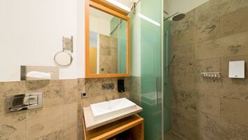 A modern bathroom with a glass shower enclosure, a wooden vanity with a white sink, and a large mirror.