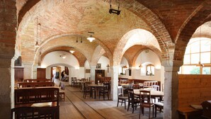 A spacious dining area with brick arches, wooden tables and benches, and hanging pendant lights.