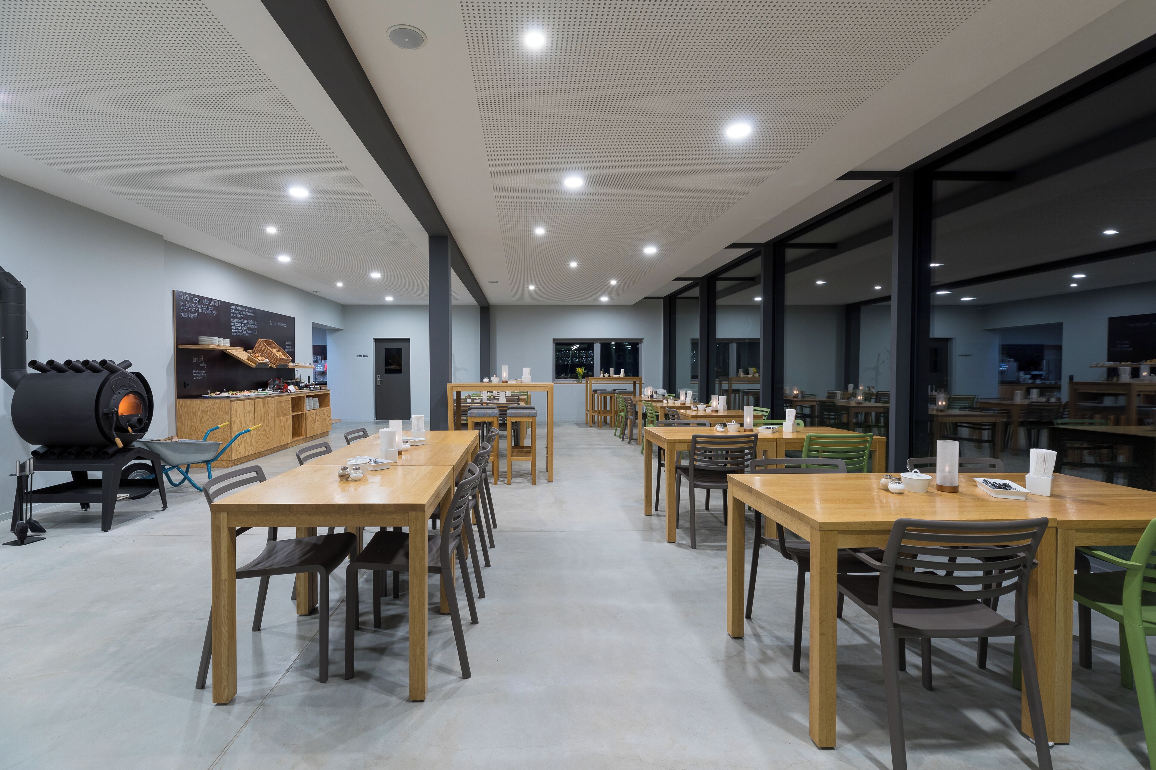 A spacious dining area with multiple wooden tables and chairs, a large black industrial-style oven, and a chalkboard menu on the wall.