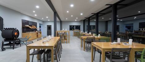 A spacious dining area with multiple wooden tables and chairs, a large black industrial-style oven, and a chalkboard menu on the wall.