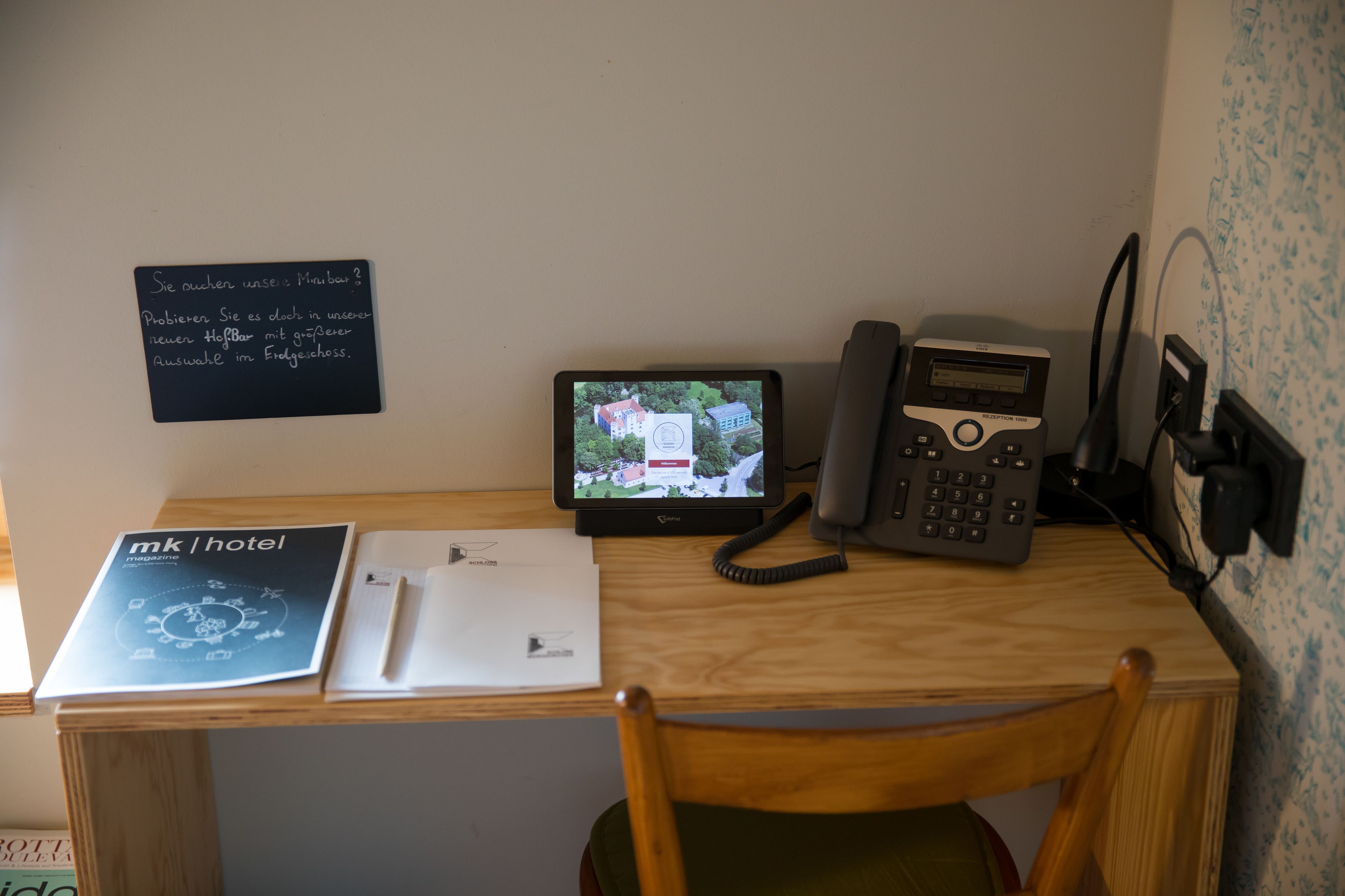 Un escritorio con un monitor de computadora, un teléfono y un documento impreso con el título 'mk hotel'.