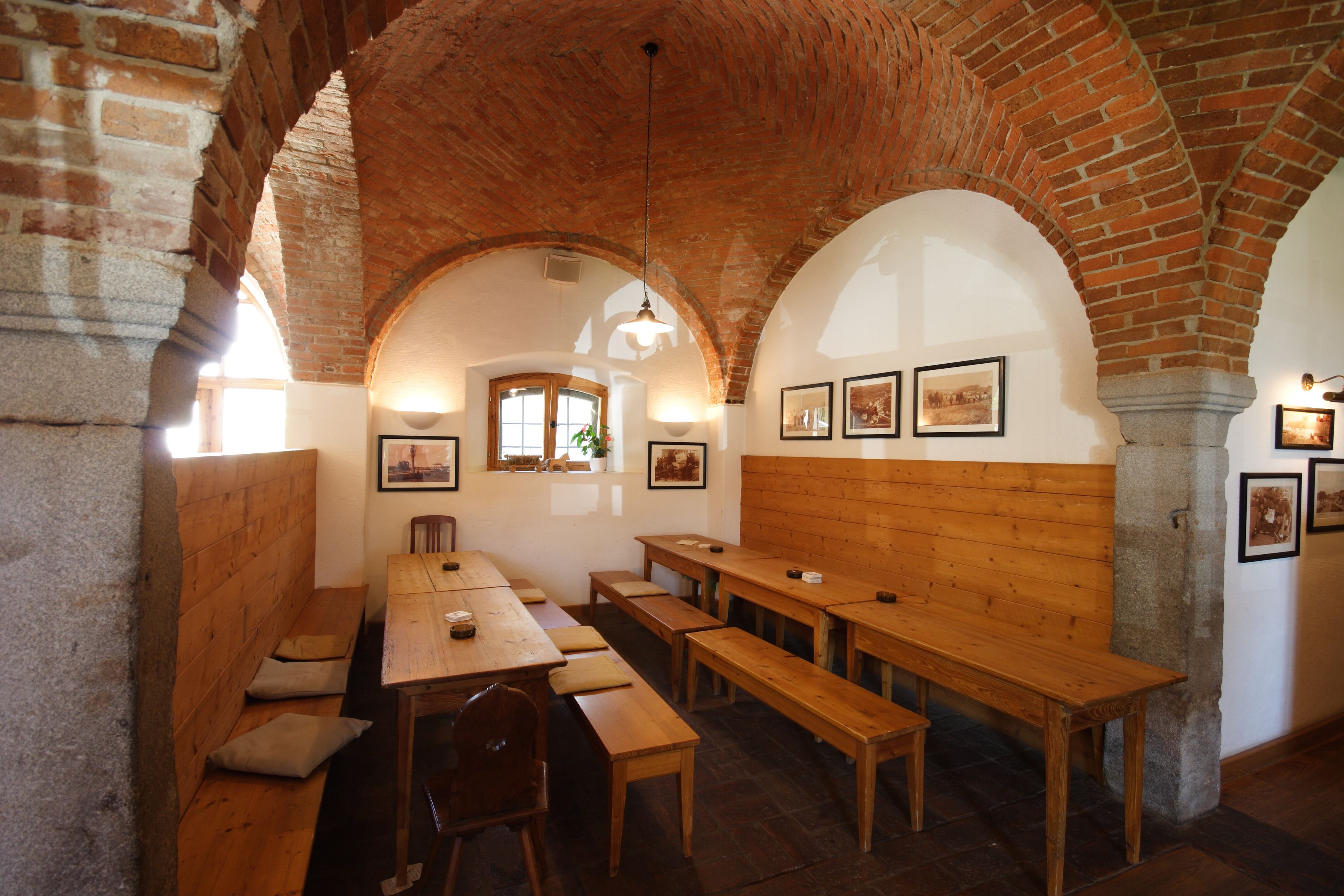 A room with wooden benches and tables, arched brick ceilings, and framed pictures on the walls.