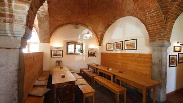 A room with wooden benches and tables, arched brick ceilings, and framed pictures on the walls.