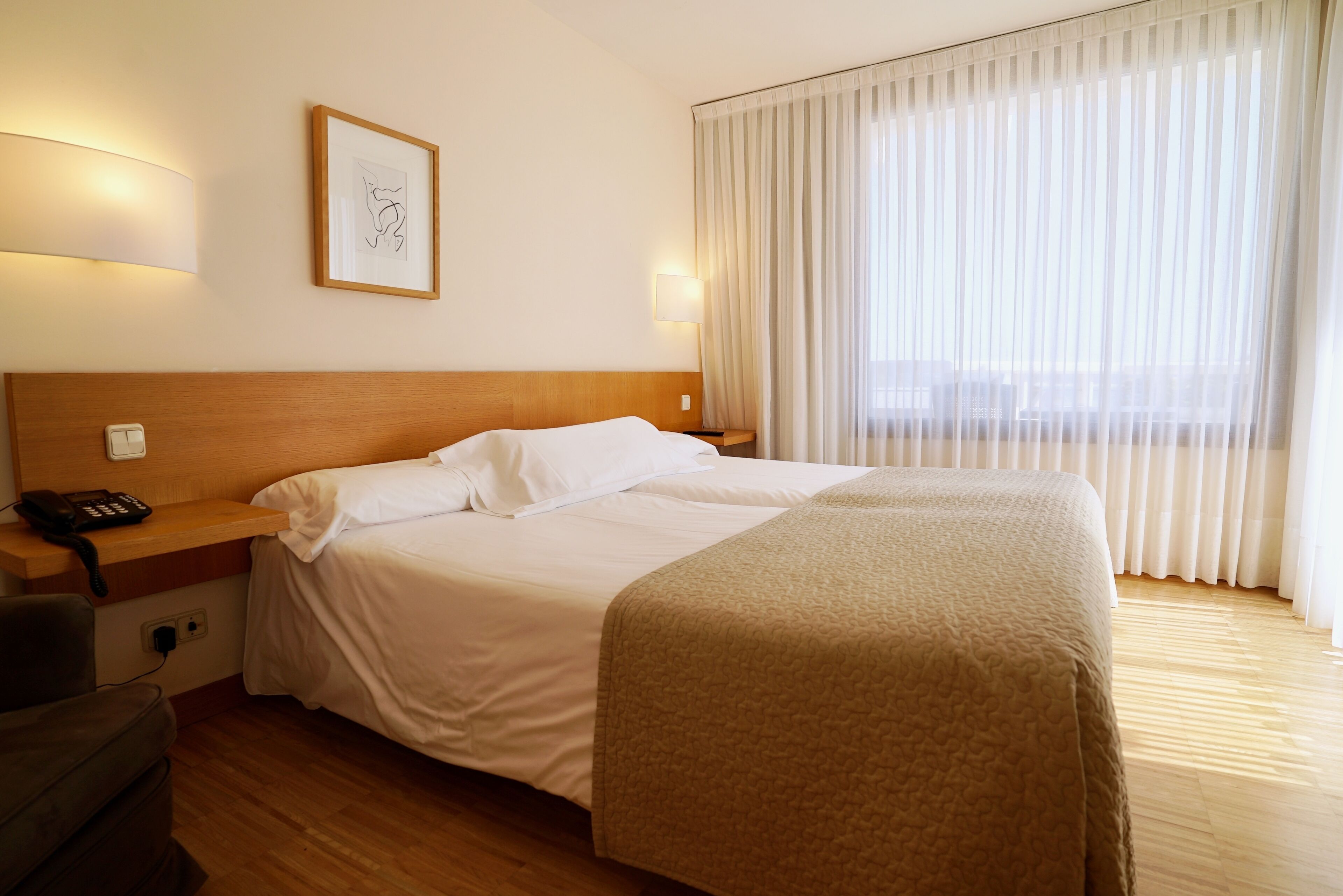 A hotel room with a large bed, a bedside table with a phone, a lamp, and a framed picture on the wall.