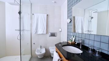 Un baño moderno con ducha de vidrio, un bidé, un inodoro y un tocador con encimera negra y espejo.