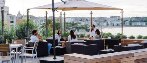 A rooftop terrace with outdoor seating, a view of the city, and a body of water in the background.