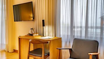 Habitación de hotel con escritorio de madera, una silla, televisor de pantalla plana y ventana con cortinas translúcidas.