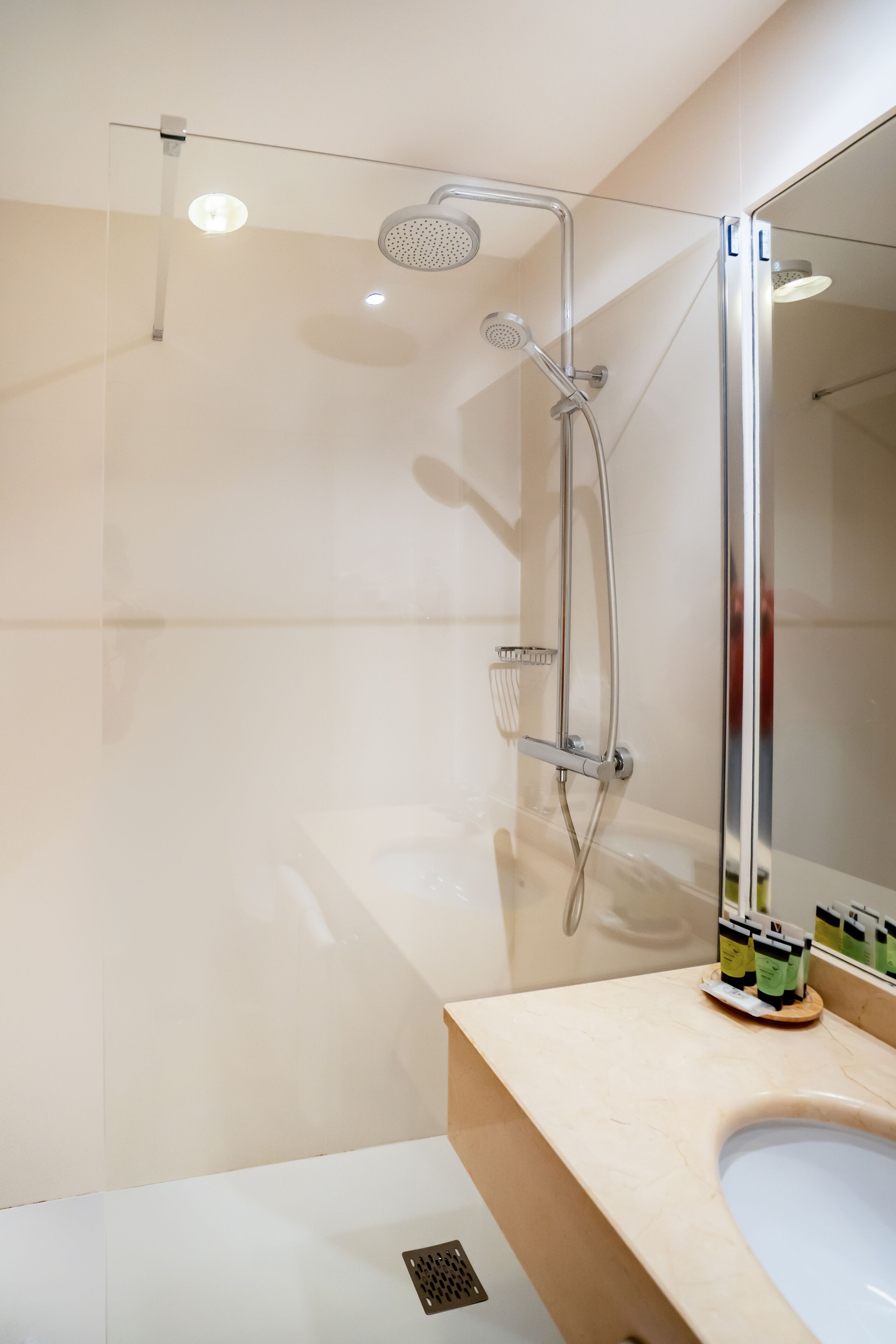 A modern bathroom with a glass-enclosed shower, a large mirror, and a beige countertop.