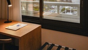 A room with a view of the beach and cityscape through a large window, a desk with a lamp, and a chair. - Gran Hotel Victoria (Santander)