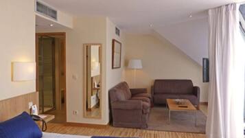 A hotel room with a bed, two armchairs, a small table, a lamp, and a mirror.
