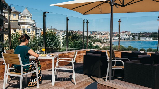 A terrace with wooden furniture and a table, overlooking a coastal cityscape. - Gran Hotel Victoria (Santander)