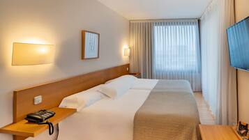 A hotel room with a bed, bedside table with a phone, a TV, and a window with curtains.