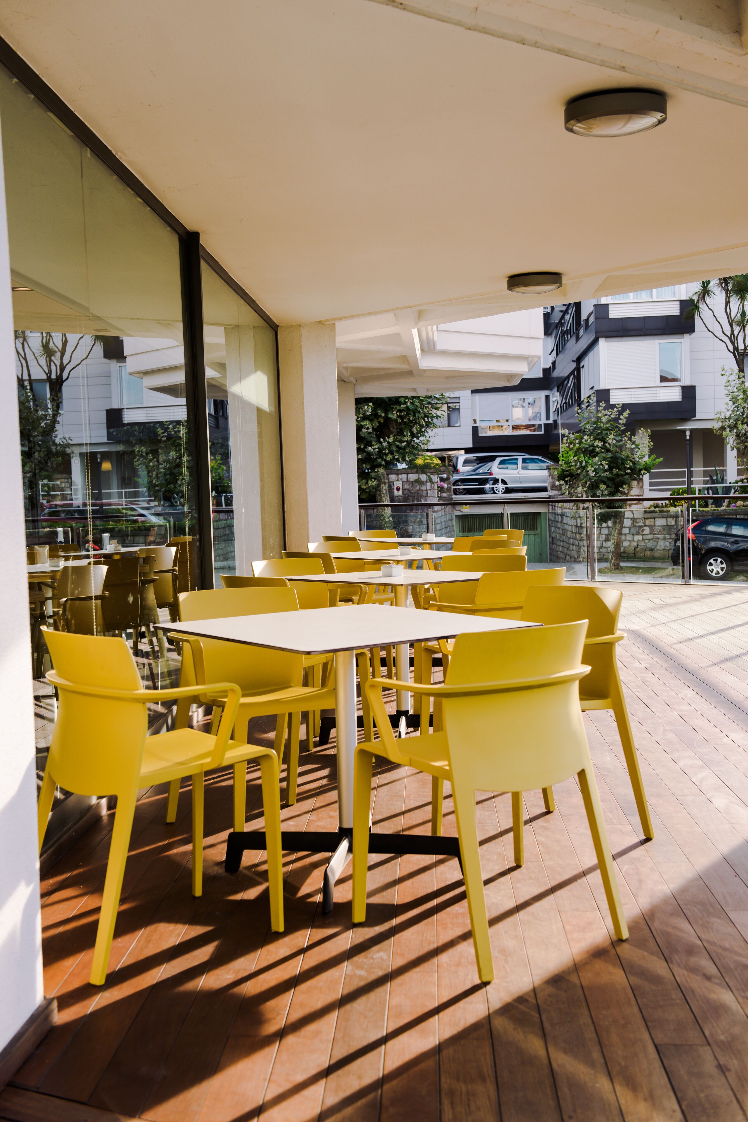 An outdoor seating area with yellow tables and chairs, large windows, and a view of the street.