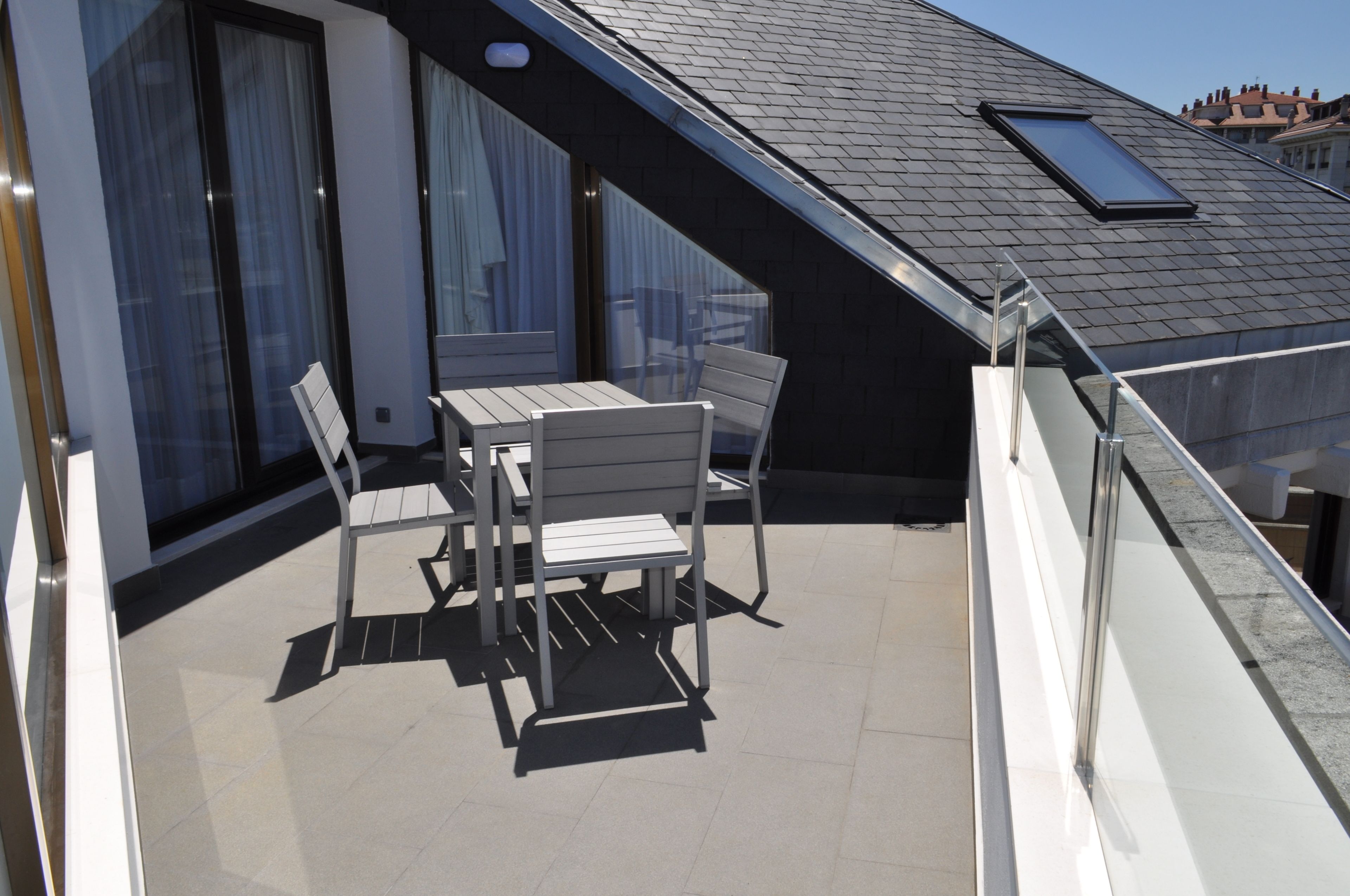 Een balkon met een tafel en stoelen, een glazen hekwerk en uitzicht op de stad.