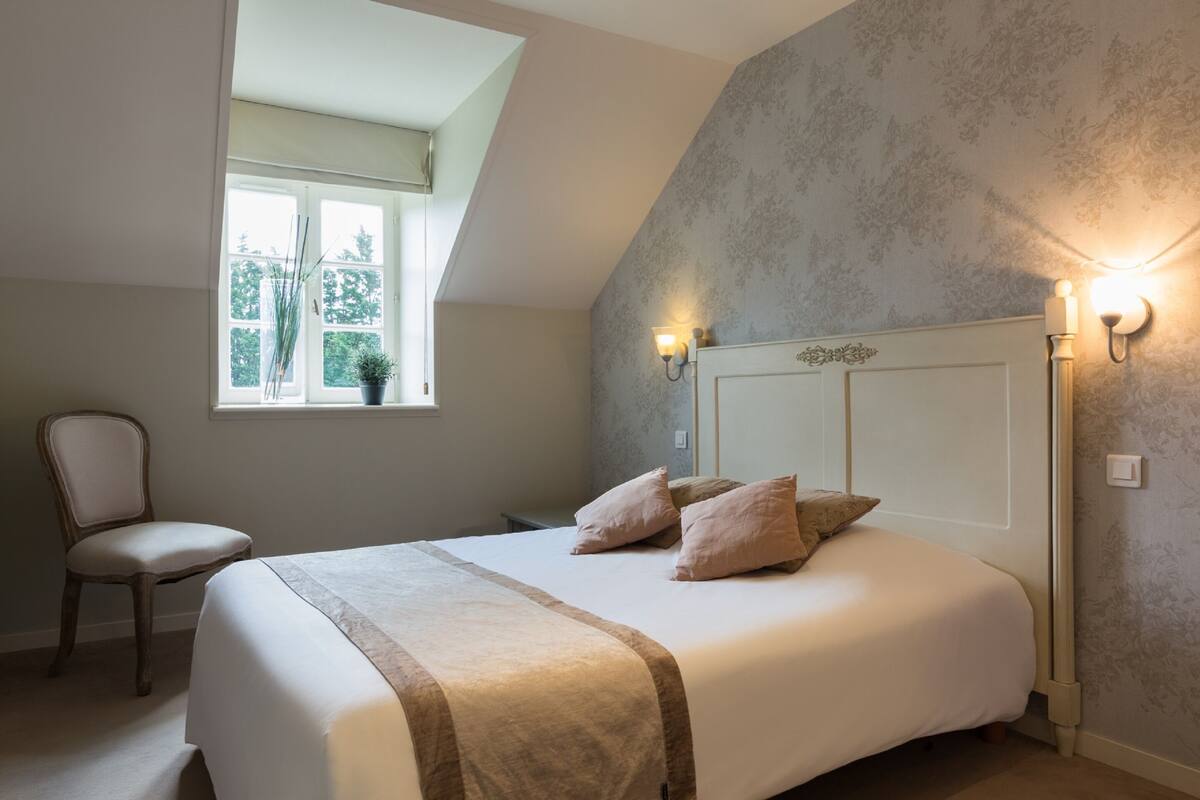 Une chambre à coucher avec un lit, une chaise, une fenêtre et des appliques murales.