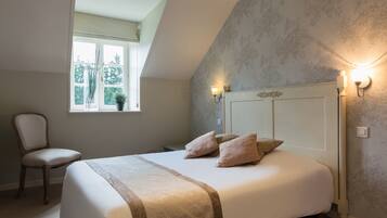 A bedroom with a bed, a chair, a window, and wall sconces.