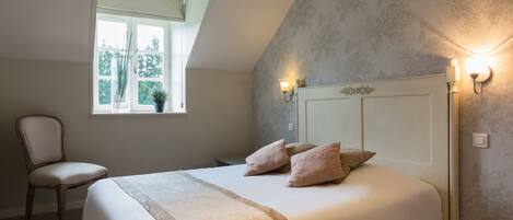 A bedroom with a bed, a chair, a window, and wall sconces.
