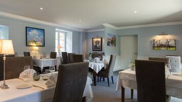 A dining area with tables set for service, chairs, and artwork on the walls.