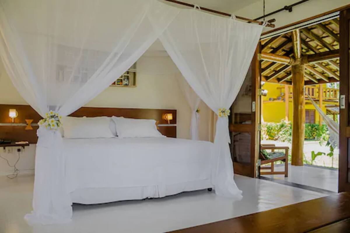 A bed with a canopy, wooden headboard, bedside tables with lamps, and a view of the outside.