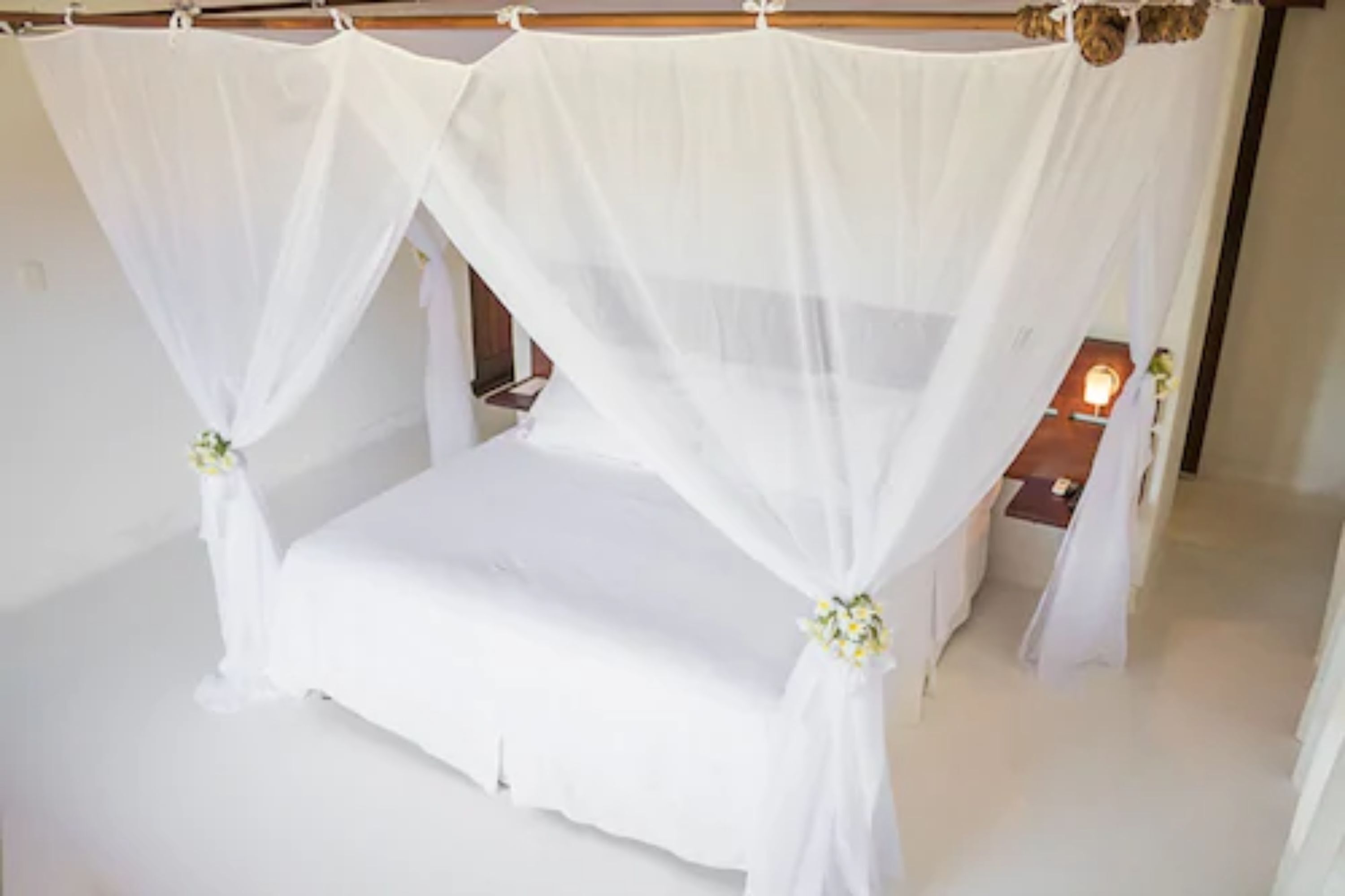 Una cama con dosel y cuatro columnas, con ropa blanca y detalles florales.