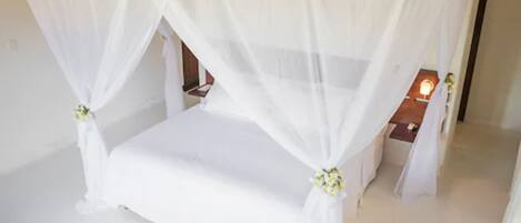 Una cama con dosel y cuatro columnas, con ropa blanca y detalles florales.
