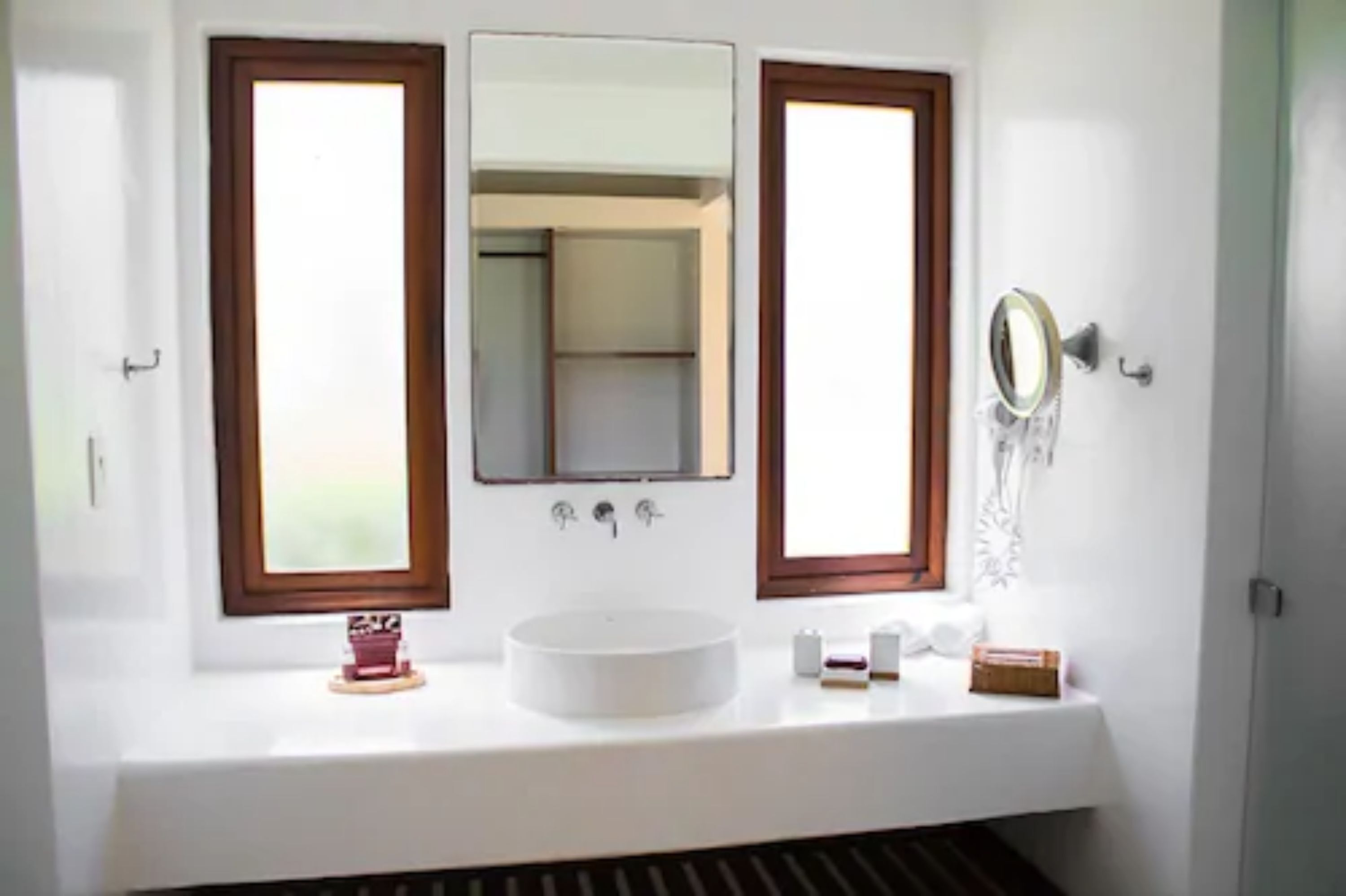 A bathroom with a white sink, two mirrors, and a window.