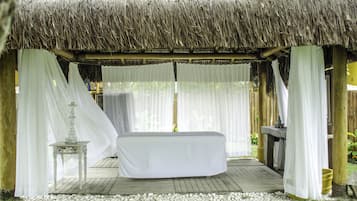 Relax in a serene outdoor space with a single bed, table, and lamp, surrounded by a wooden deck and pebbles.