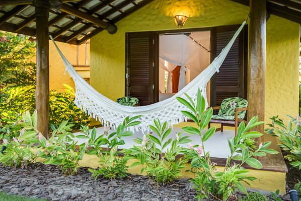 Una hamaca bajo una pérgola de madera, una silla de madera y una mesita con una planta.