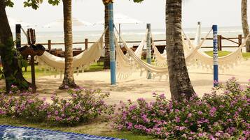 Una playa con hamacas, una piscina y flores rosadas.