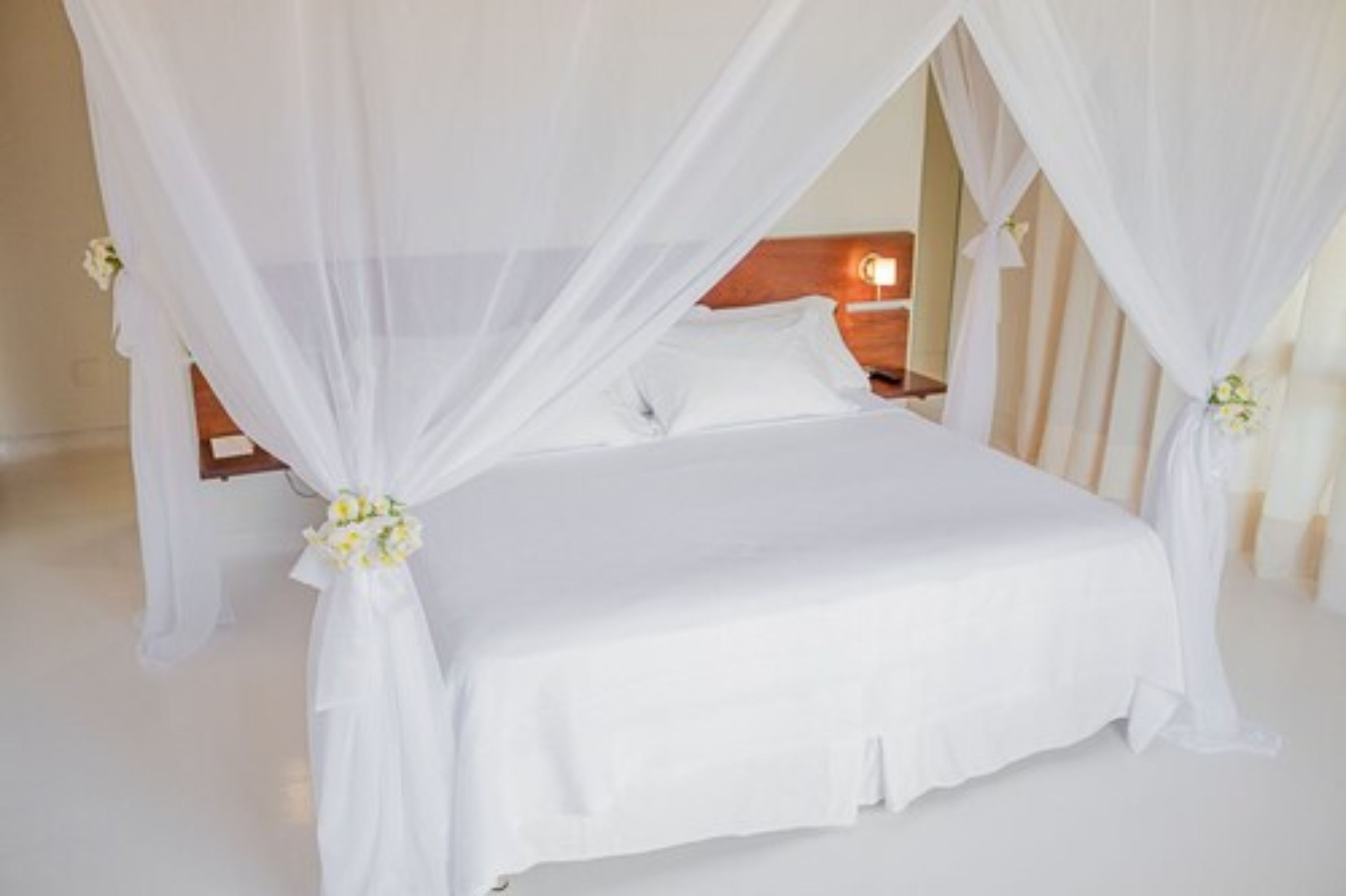 A bed with a canopy, white bedding, and a floral arrangement on the bed.