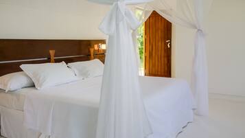 Quarto com cama de dossel, cabeceira de madeira e vista para o exterior.