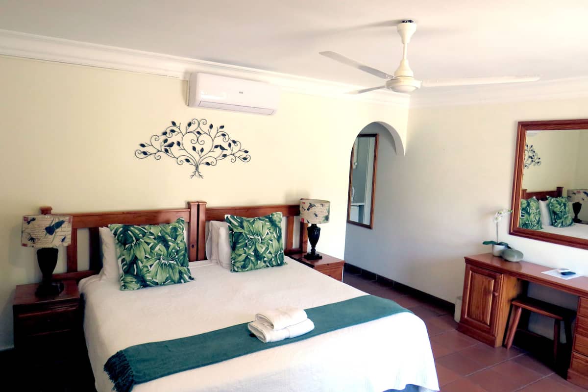 A hotel room with a bed, a desk, a mirror, and a ceiling fan.