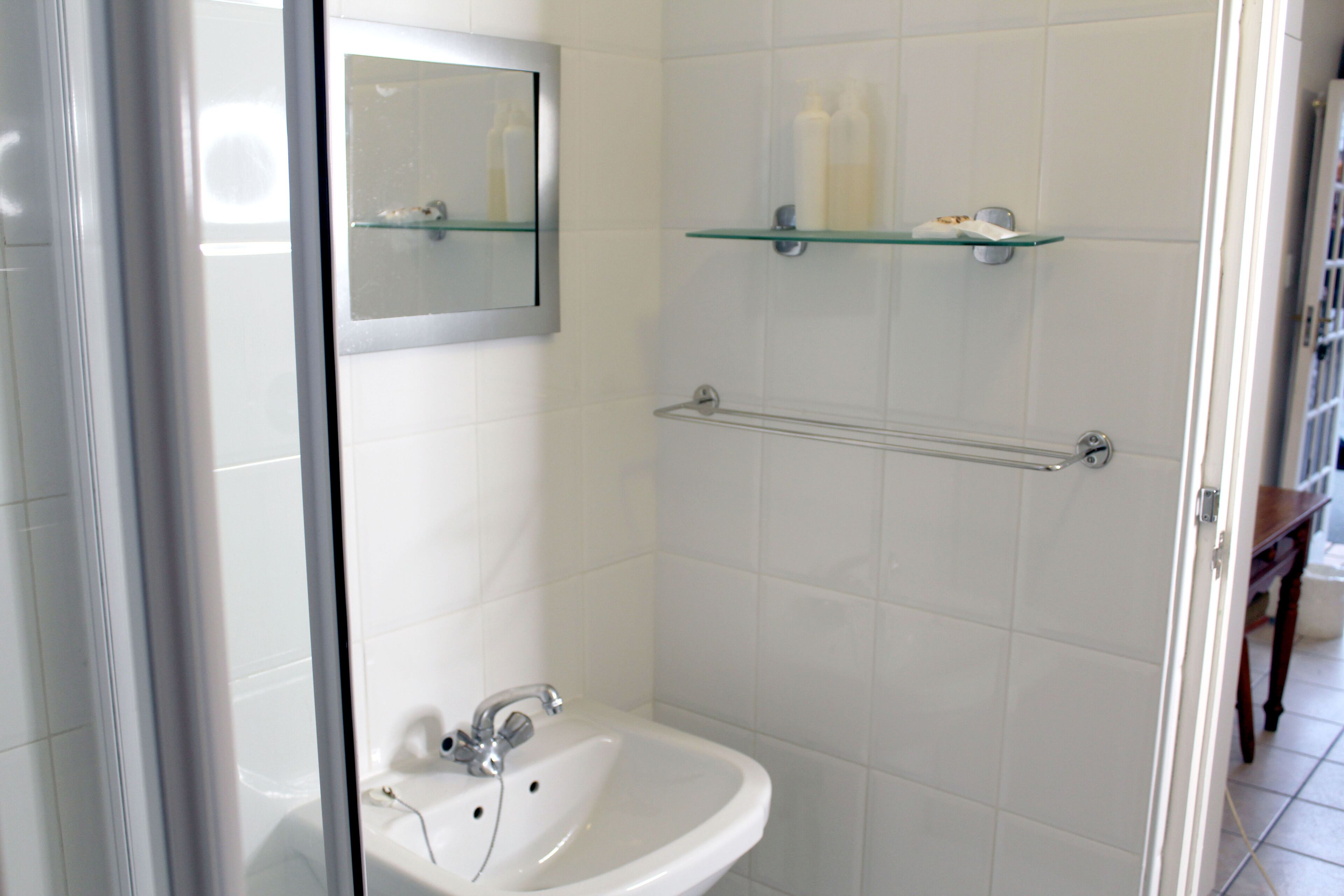 Un baño con un lavabo blanco, un espejo y dos repisas de vidrio sobre el lavabo.
