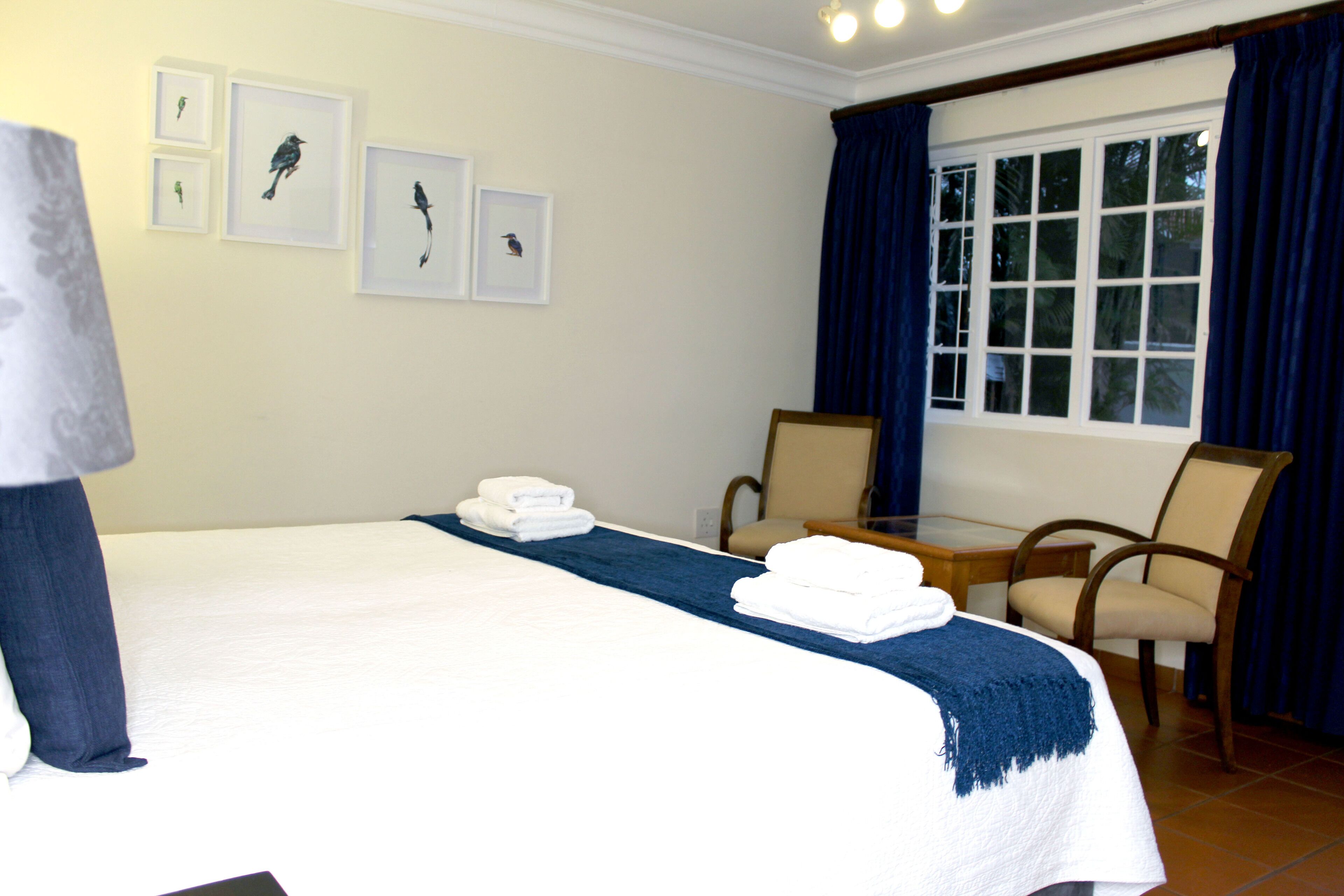 A hotel room with a bed, two chairs, a table, and framed pictures on the wall.