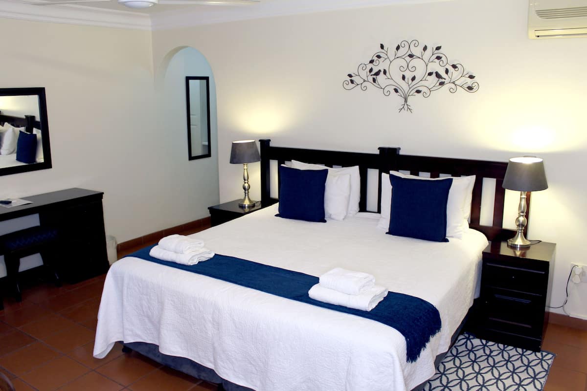 A neatly made bed with white and blue bedding, two bedside tables with lamps, a wall mirror, and a decorative wall piece.