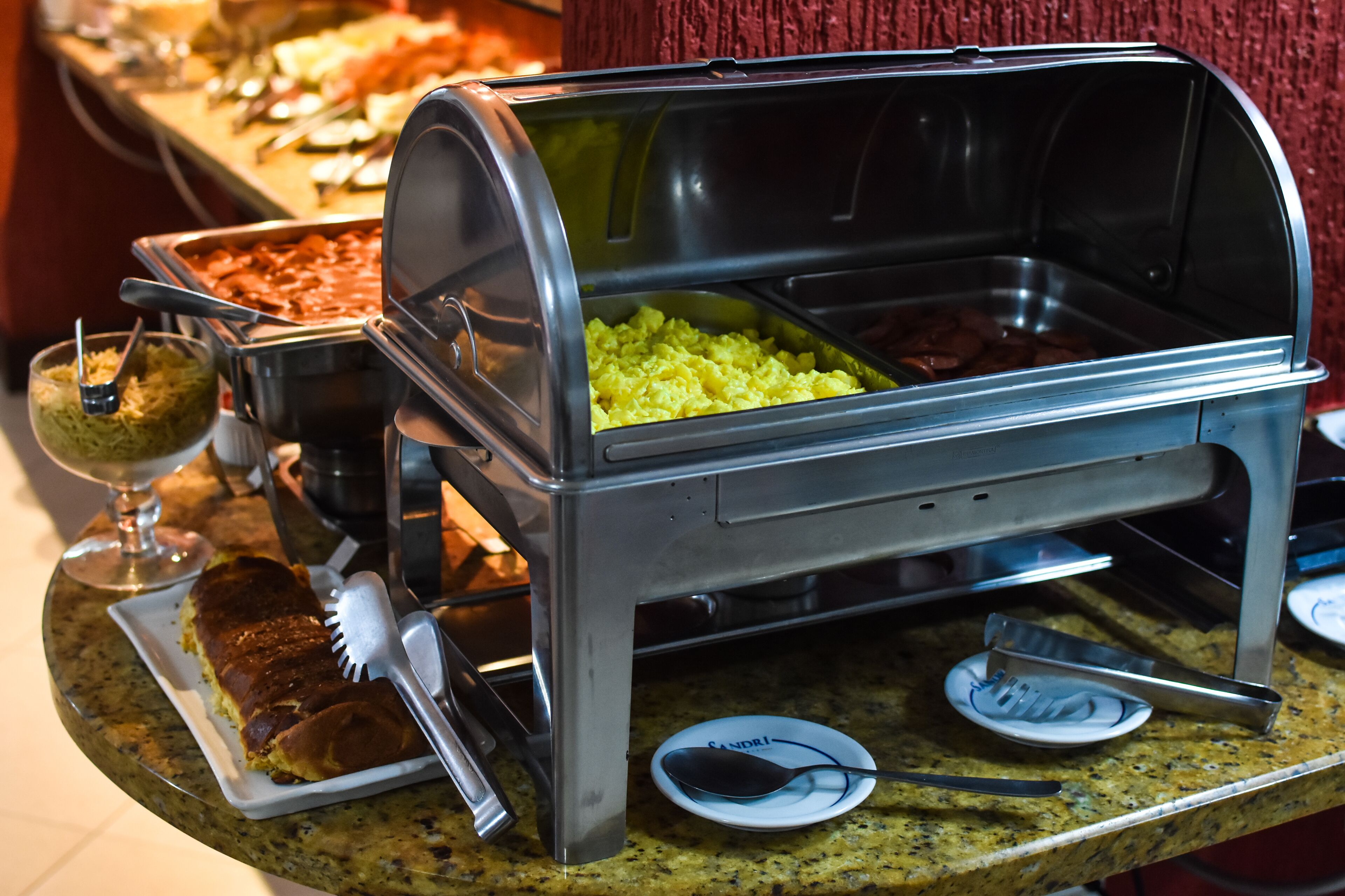Een buffetopstelling met diverse gerechten en bestek op een granieten aanrecht.