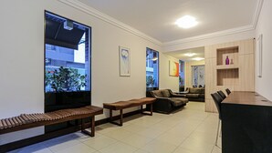 A modern living room with a sofa, a wooden bench, a dining table with chairs, and large windows with a view of buildings.