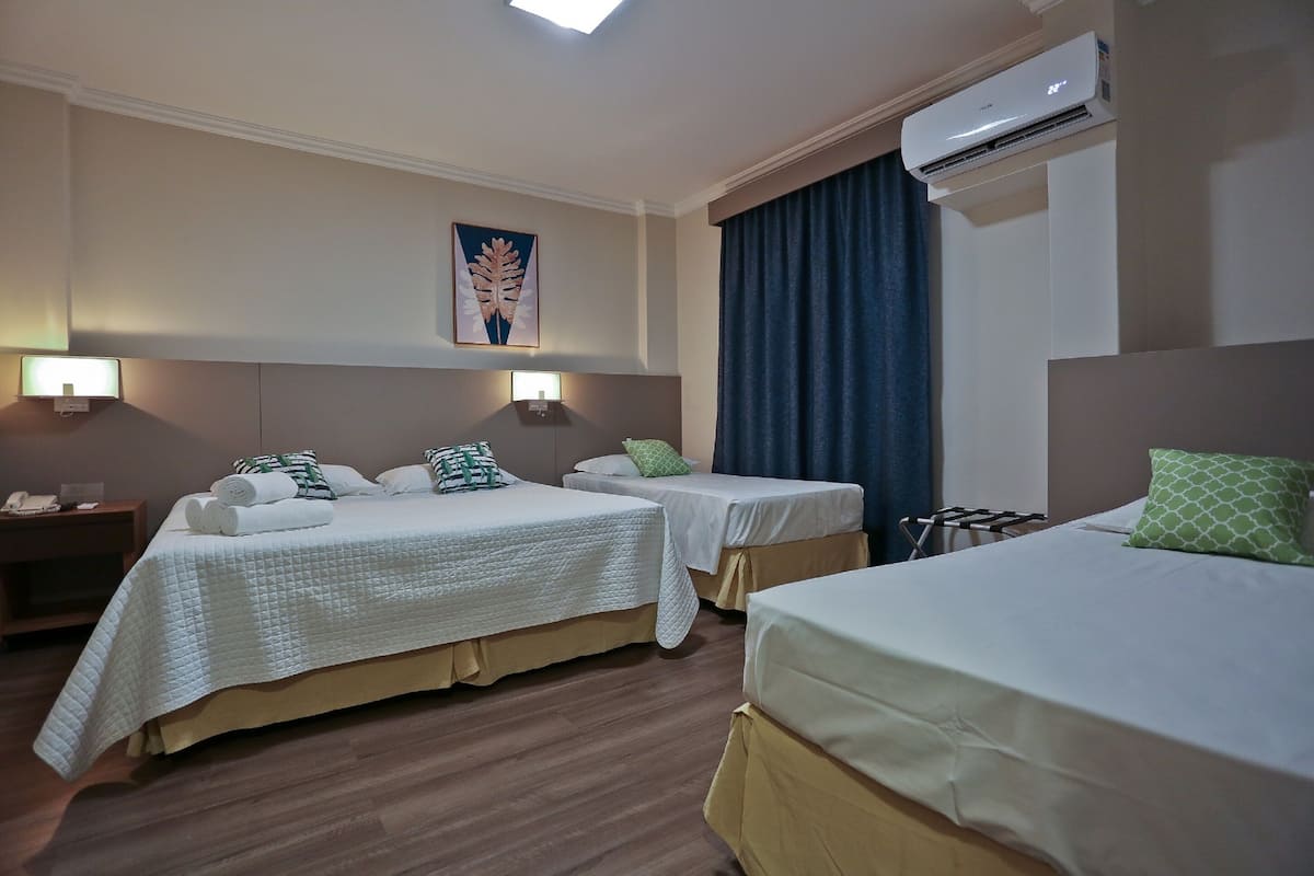 A hotel room with two single beds, a nightstand with a lamp, an air conditioner, and a painting on the wall.