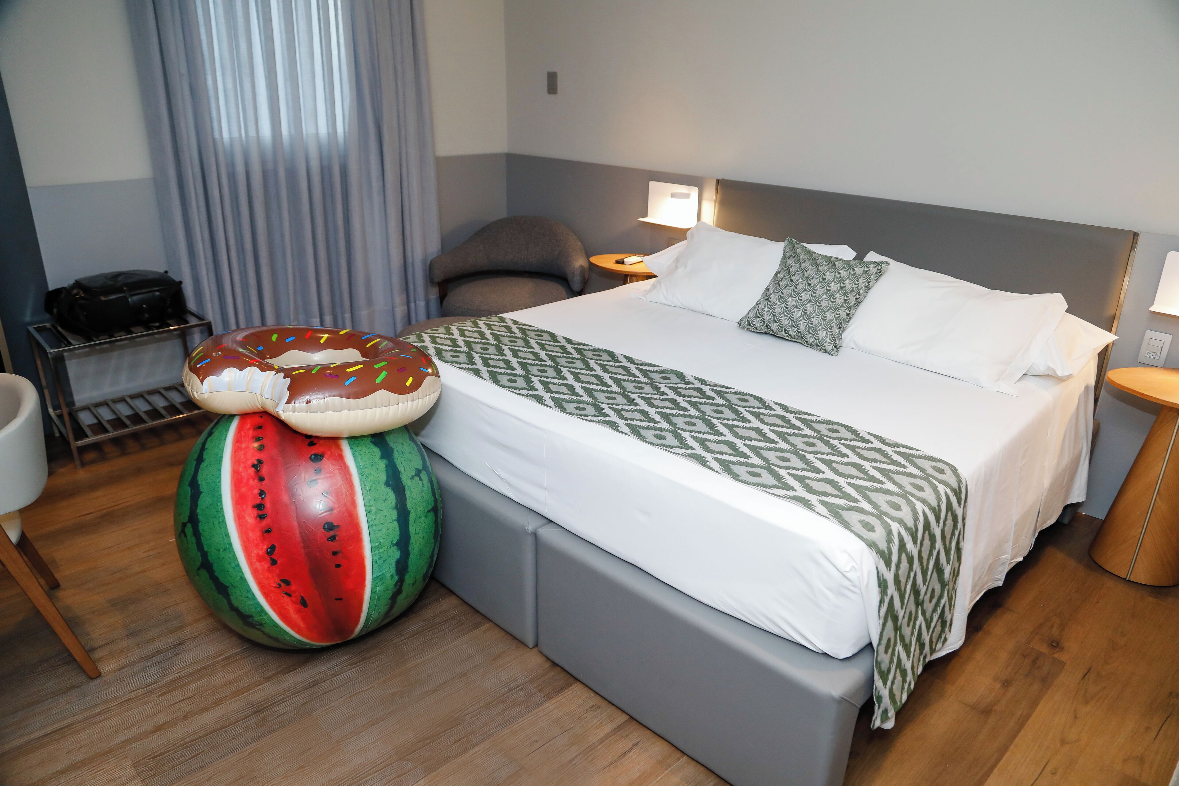 A hotel room with a bed, a large watermelon-shaped stool, a chair, a desk, and a lamp.