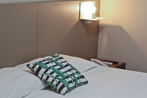 Una cama bien hecha con ropa blanca y un cojín decorativo con diseño de hojas.