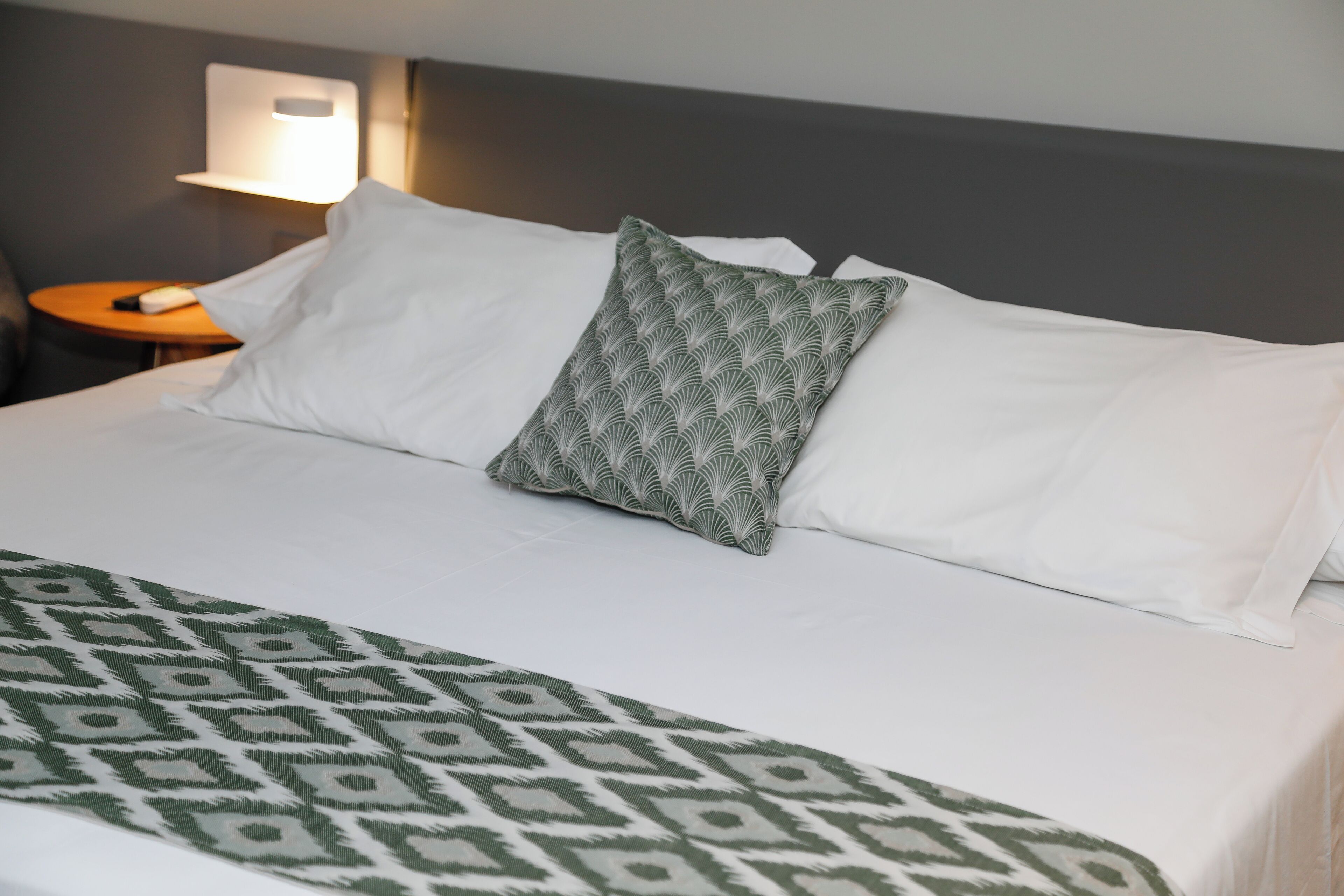 A neatly made bed with white linens and a patterned throw blanket.