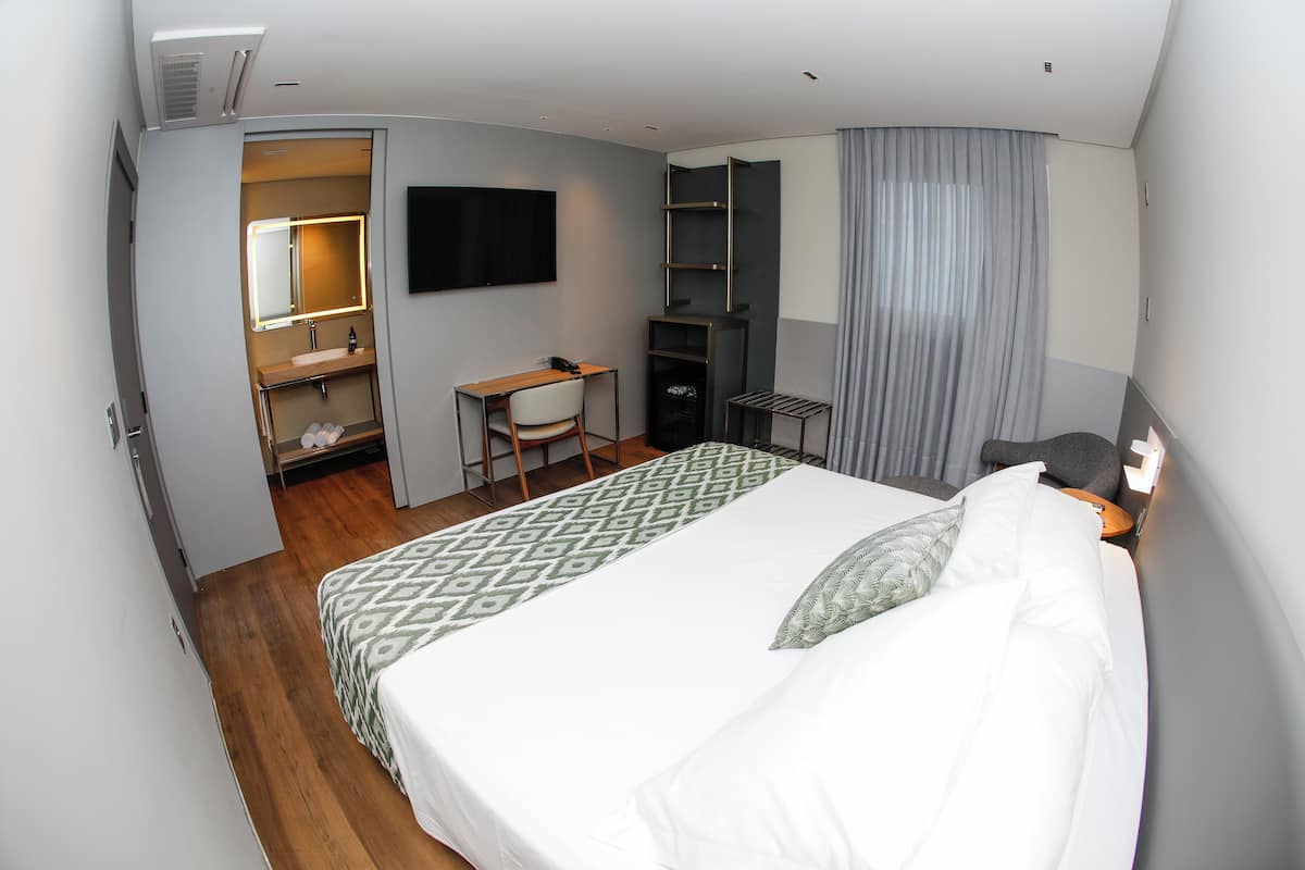 A hotel room with a bed, a desk, a chair, a TV, and a wardrobe.