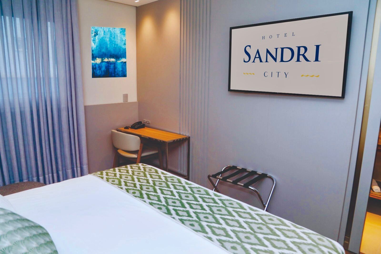 Una habitación de hotel con una cama, un escritorio, una silla, un televisor montado en la pared y un cartel que dice 'HOTEL SANDRI CITY'.