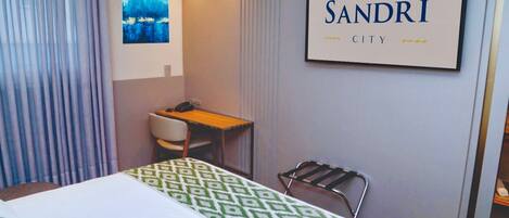 Una habitación de hotel con una cama, un escritorio, una silla, un televisor montado en la pared y un cartel que dice 'HOTEL SANDRI CITY'.