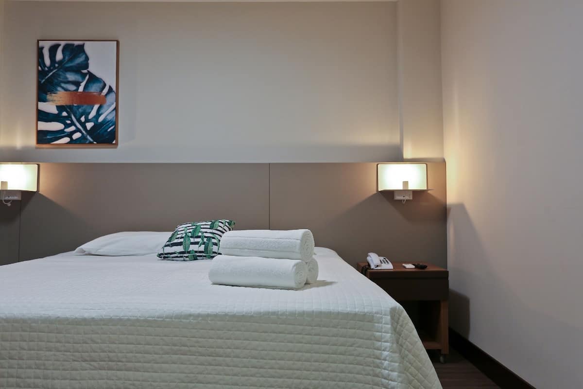 A neatly made bed with white linens and a green patterned pillow, two bedside lamps, and a framed artwork on the wall.