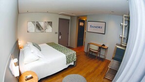 A hotel room with a bed, a desk, a chair, and a small table.