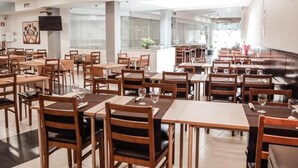 Ein geräumiges Restaurant mit mehreren Tischen und Stühlen, einem an der Wand befestigten Flachbildfernseher und einem großen Fenster, das für natürliches Licht sorgt.