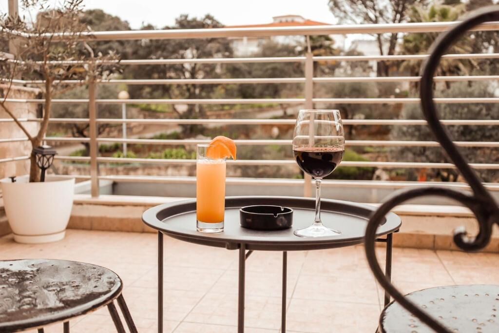 Un balcon avec une table, un verre de vin rouge et un grand verre de jus d’orange.