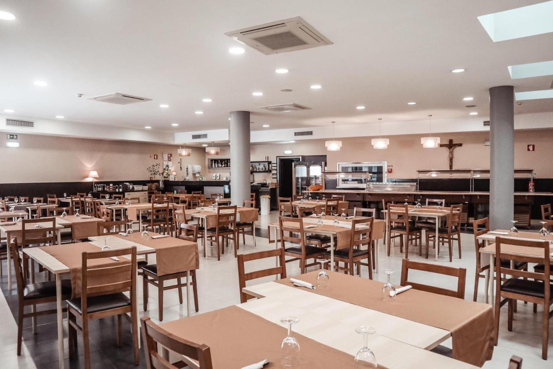 Un grand espace dédié à la salle à manger, avec plusieurs tables et chaises, un coin cuisine à l’arrière-plan et une croix accrochée au mur.
